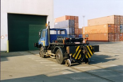 2-Wege-Unimog U1450 im Firmengelände vor klassischer Hafenkulisse