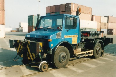 2-Wege-Unimog U1450 im Firmengelände vor klassischer Hafenkulisse